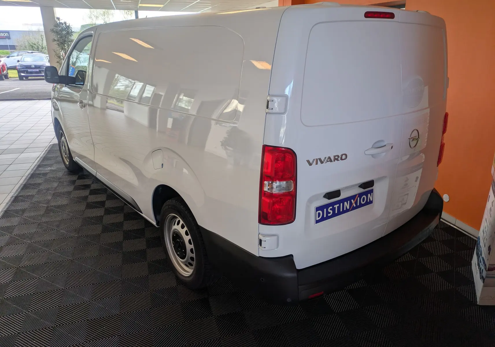Vue 3/4 arrière droite d’un Opel Vivaro Fourgon blanc Icy avec jantes tôle 17 pouces dans un showroom.