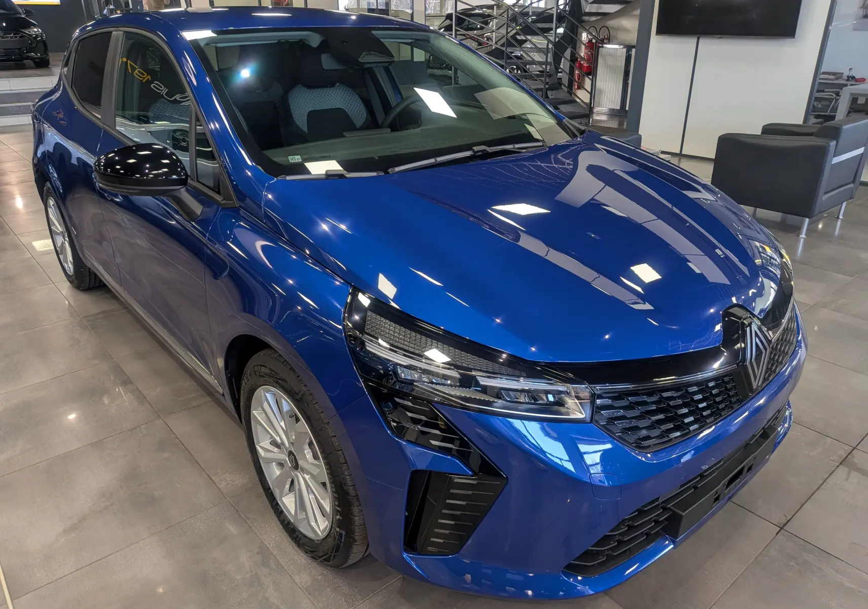 Renault Clio V Blue dCi 100 en bleu Iron, vue 3/4 avant droit, avec calandre noire et phares LED distinctifs.