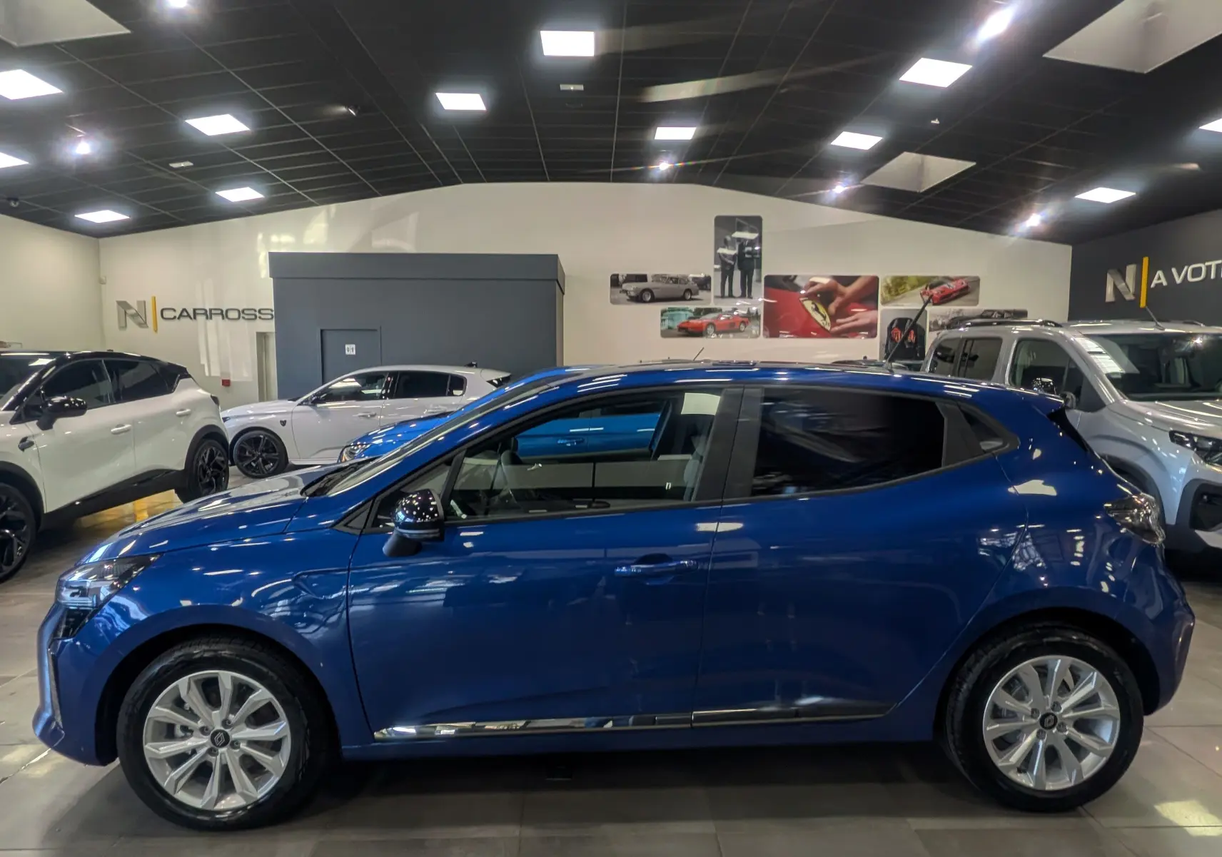Profil droit d'une Renault Clio V bleu Iron 2025 en finition Evolution, visible en intérieur de showroom lumineux.