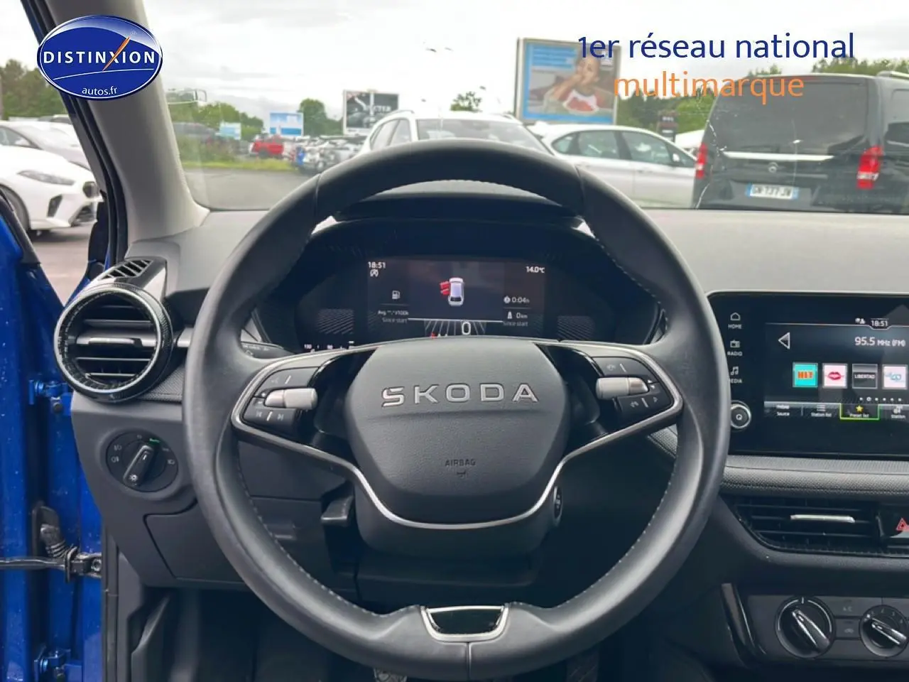 Vue intérieure centrée sur le volant cuir SKODA d'une Fabia bleue avec écran tactile et commandes au volant visibles.