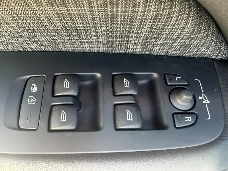 Gros plan sur les commandes de lève-vitres et réglage des rétroviseurs côté conducteur du Volvo S60 gris Platinium 2024.