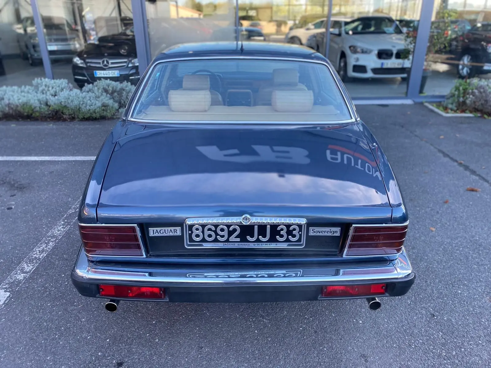 Vue arrière d'une Jaguar XJ6 3.6 Sovereign bleue de 1987 avec plaques noires et feux rectangulaires rouges.