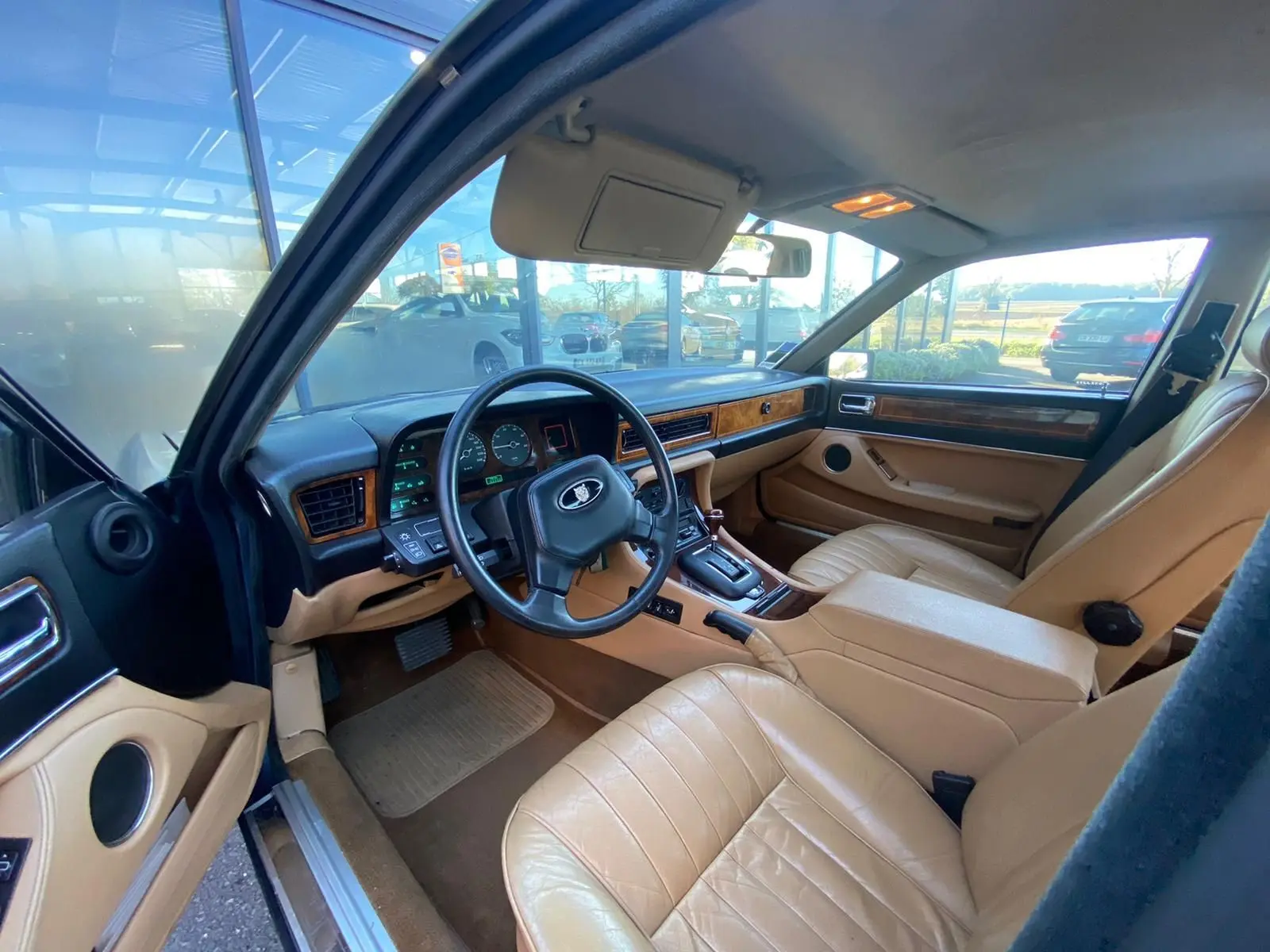 Vue intérieure côté conducteur d'une Jaguar XJ6 3.6 Sovereign 1987 bleu, avec sièges cuir beige et tableau de bord bois.