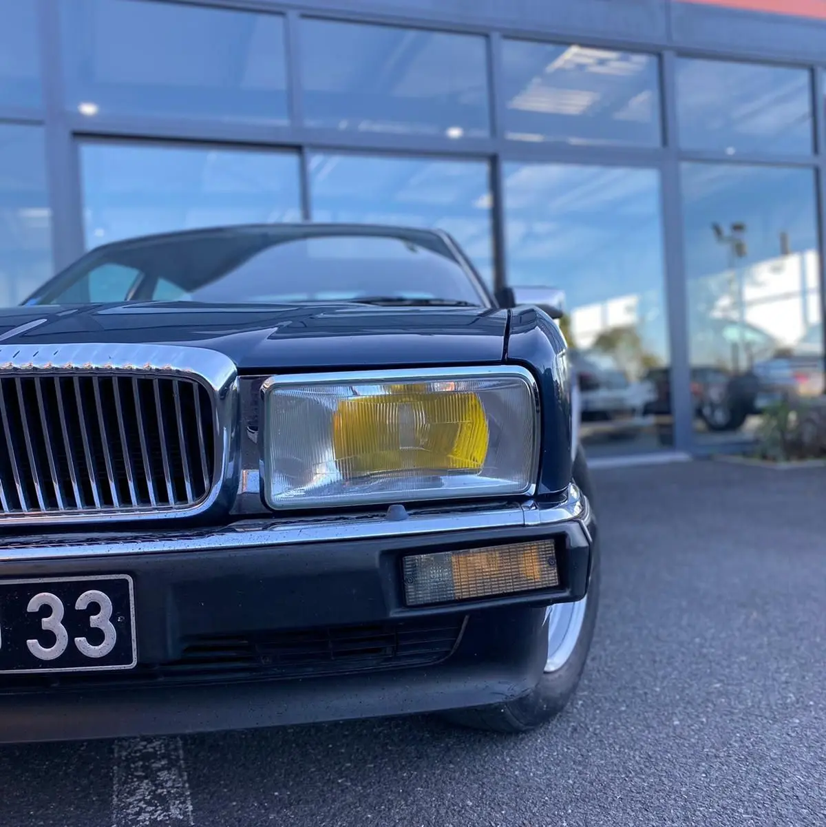 Gros plan sur l'avant droit bleu d'une Jaguar XJ6 3.6 Sovereign 1987, mettant en valeur le phare jaune et la calandre chromée.