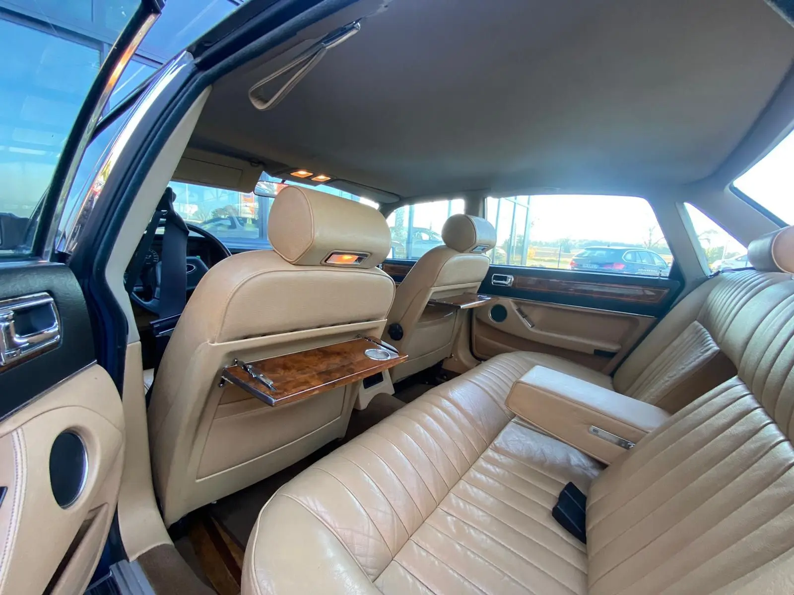 Intérieur beige cuir de la Jaguar XJ6 3.6 Sovereign 1987, vue arrière côté gauche avec tablettes en bois sur les sièges avant.