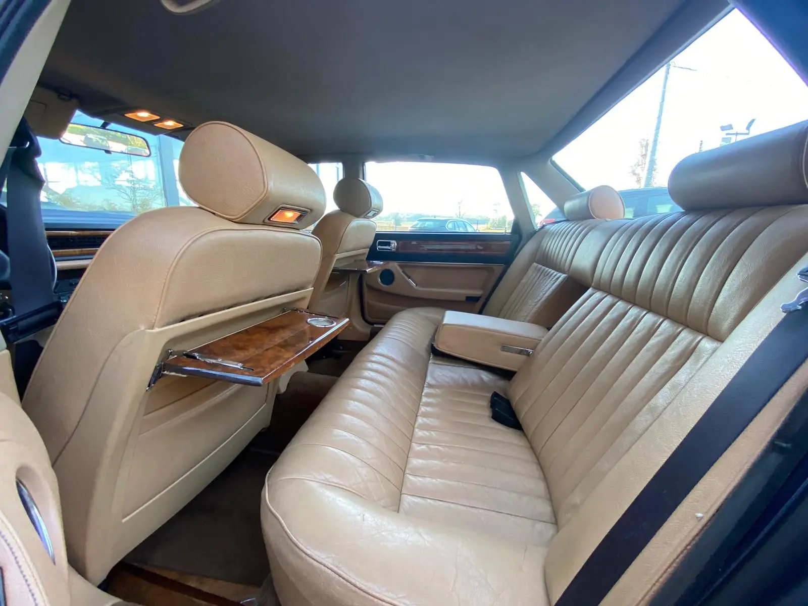 Vue intérieure arrière montrant les sièges en cuir beige et les plateaux en bois sur une Jaguar XJ6 3.6 Sovereign bleu de 1987.