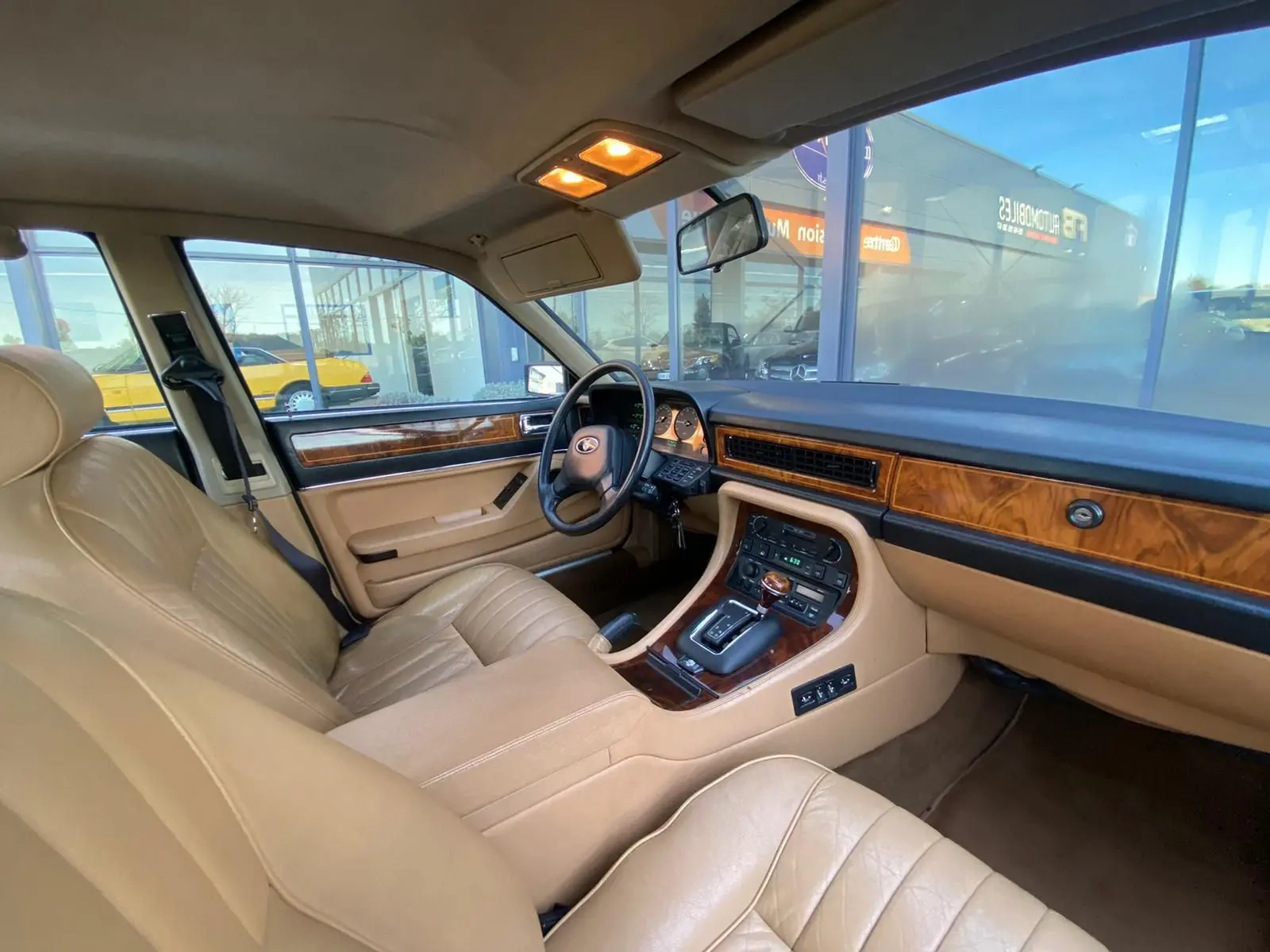 Intérieur beige clair de la Jaguar XJ6 3.6 Sovereign 1987, vue côté conducteur avec tableau de bord en bois et boîte auto.
