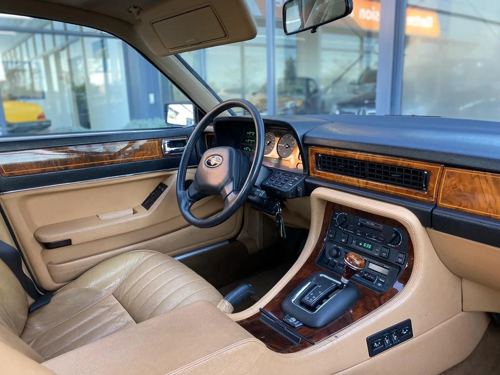 Intérieur beige et bois d'une Jaguar XJ6 3.6 Sovereign 1987, vue côté conducteur sur tableau de bord et console centrale.