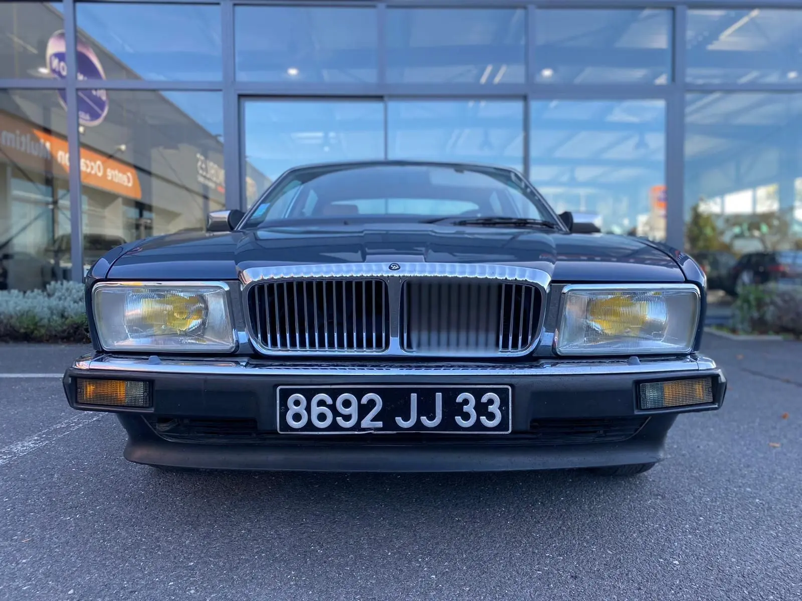Vue frontale d'une Jaguar XJ6 3.6 Sovereign bleu de 1987 avec calandre chromée et phares jaunes.