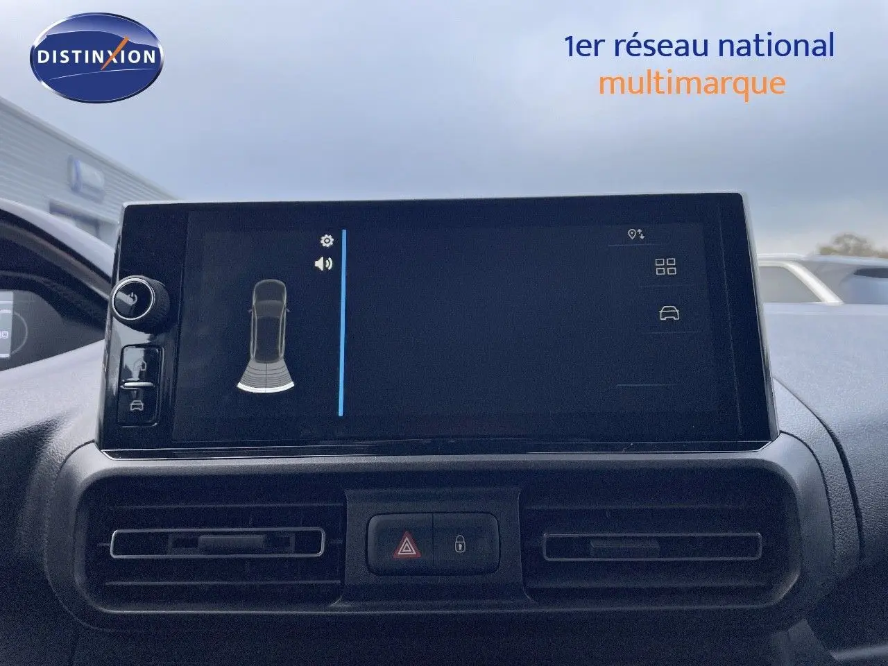 Écran tactile central du Peugeot Partner 2025 affichant l’aide au stationnement, avec les aérateurs et boutons de sécurité en dessous.