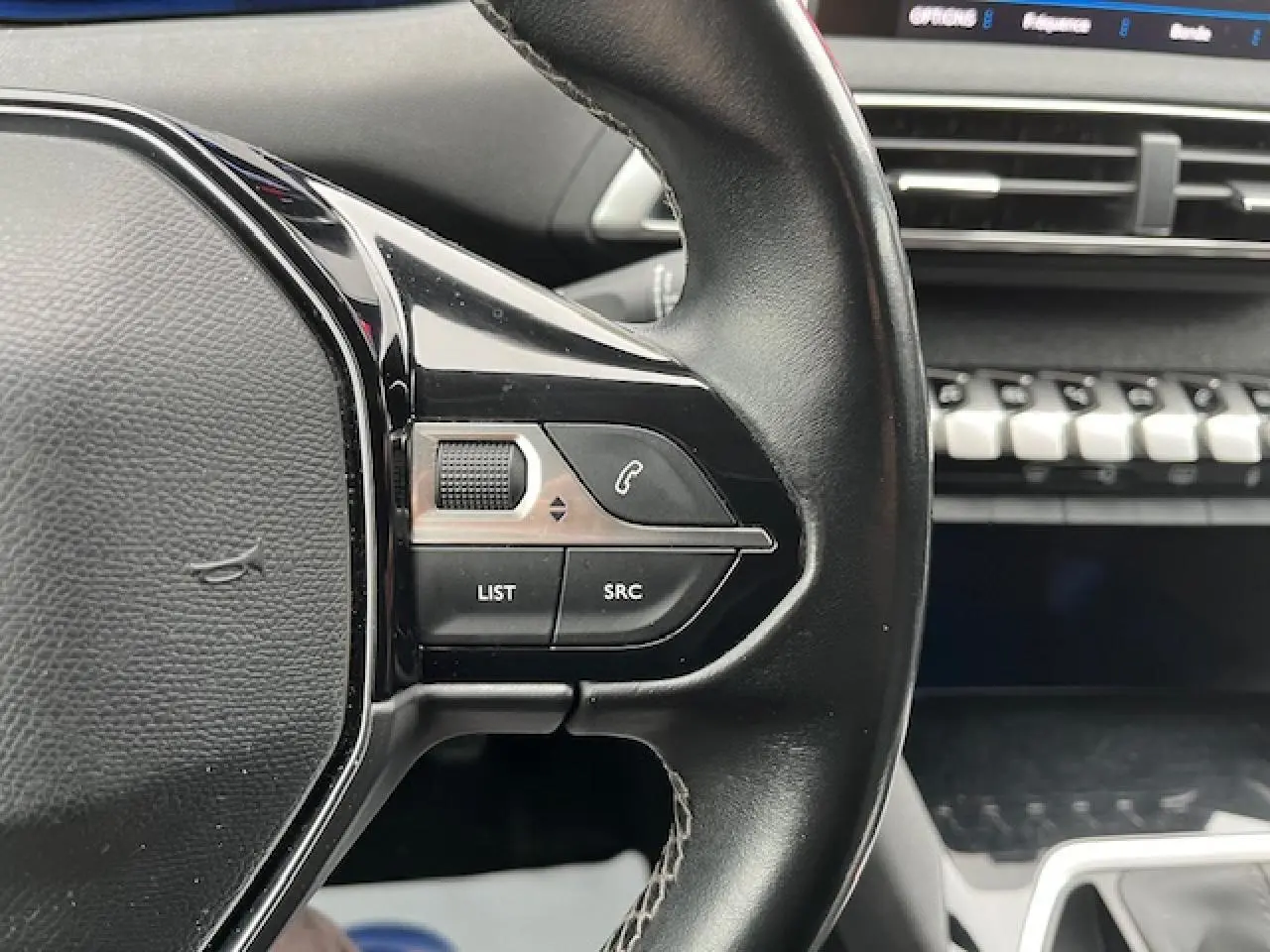 Gros plan sur le volant multifonctions en cuir du Peugeot 3008 gris Amazonite, avec commandes audio et téléphone visibles.