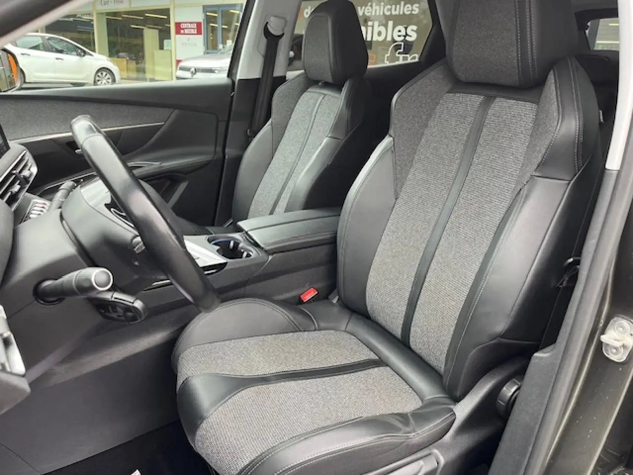 Intérieur du Peugeot 3008 2019, vue côté conducteur sur sièges semi-cuir gris et volant multifonctions.