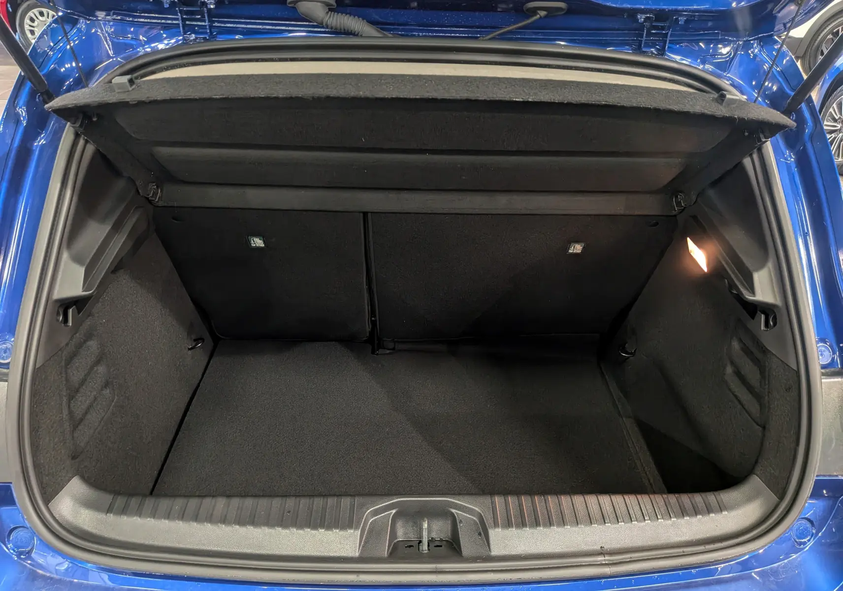 Coffre ouvert vu de l'arrière d'une Renault Clio V Bleu Iron, montrant l'espace de rangement et la lumière intérieure.