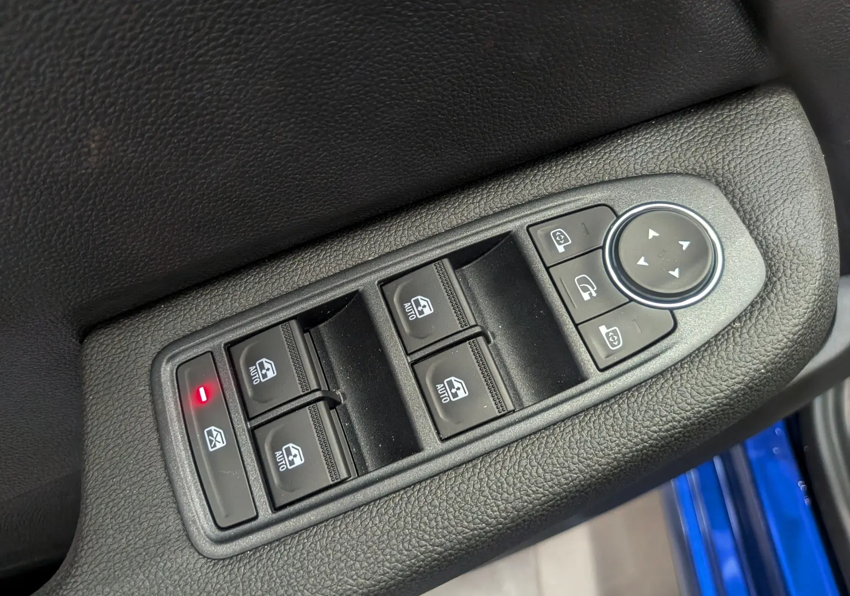 Gros plan sur les commandes des vitres et rétroviseurs côté conducteur d’une Renault Clio V Bleu Iron, intérieur noir.