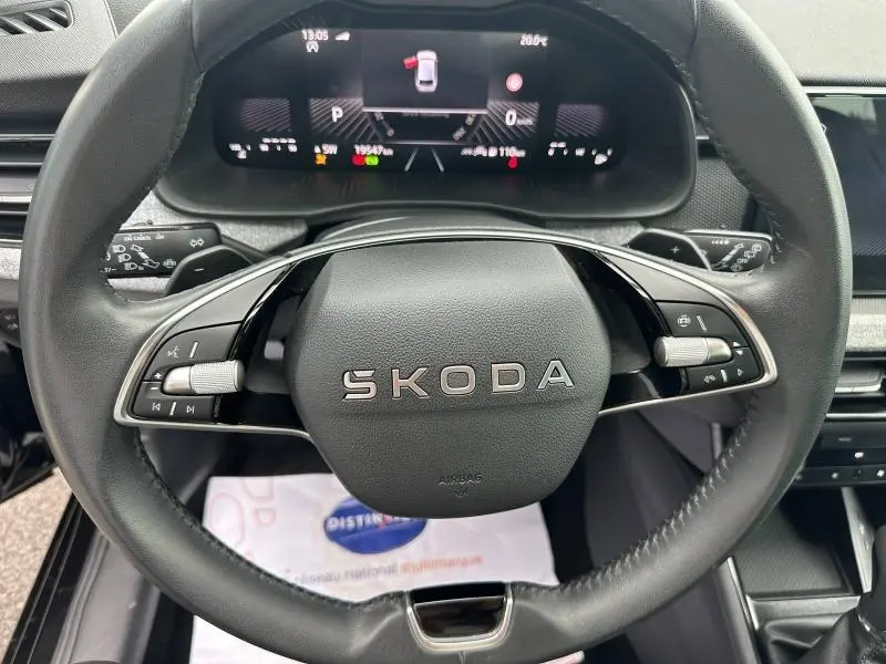 Vue rapprochée du volant cuir noir SKODA avec commandes multifonctions et tableau de bord numérique allumé.
