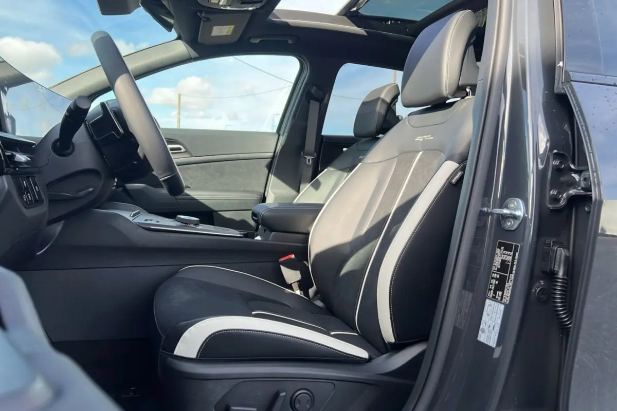 Vue intérieure côté conducteur du Kia Sportage gris eclipse avec sièges sport noirs et toit panoramique ouvert.