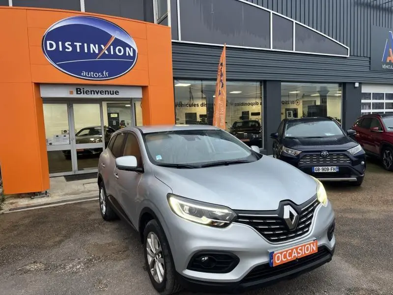 Renault Kadjar blanc en 3/4 avant droit, phares allumés, garé devant un concessionnaire Distinxion.
