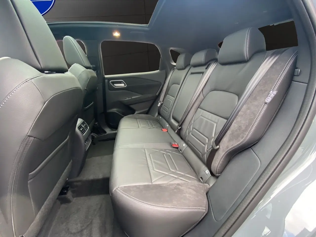 Vue intérieure arrière du Nissan Qashqai 2025, sièges en cuir noir avec surpiqûres blanches et ceintures de sécurité visibles.