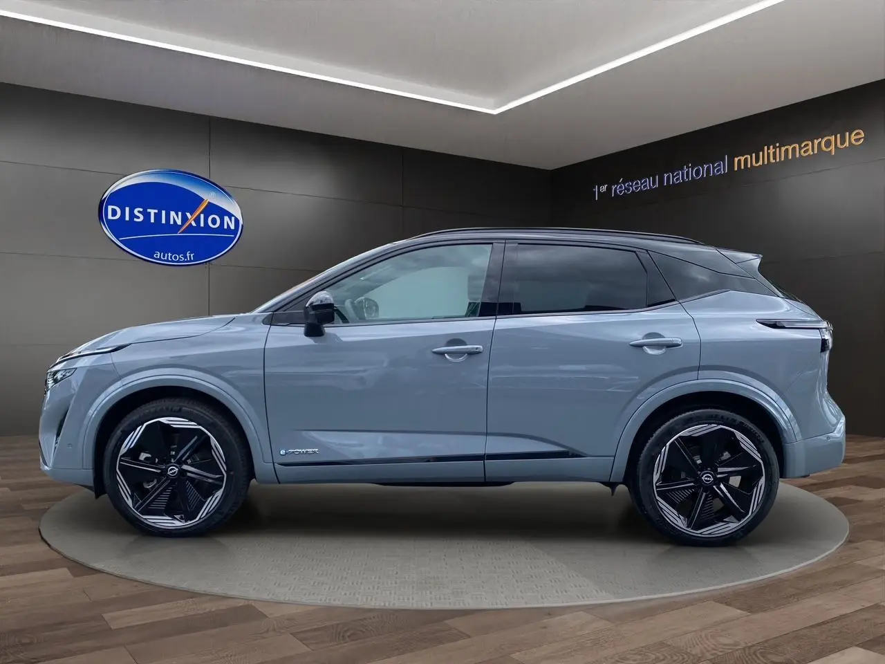 Profil côté gauche du Nissan Qashqai 1.5 e-POWER 190 BVA N-DESIGN gris ceramic avec toit noir en showroom.