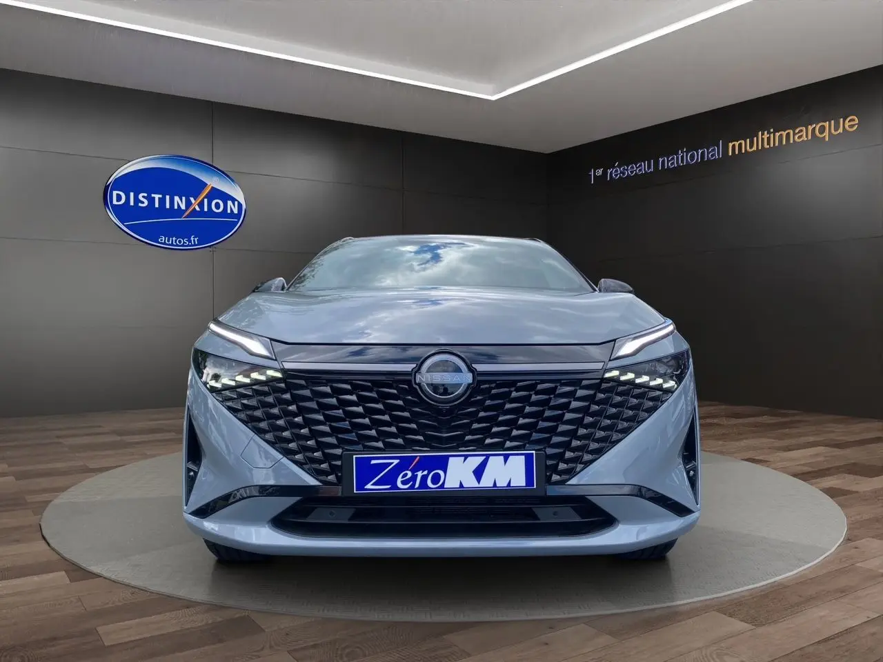 Vue frontale du Nissan Qashqai 2025 gris céramic avec calandre noire texturée et phares LED fins allumés.