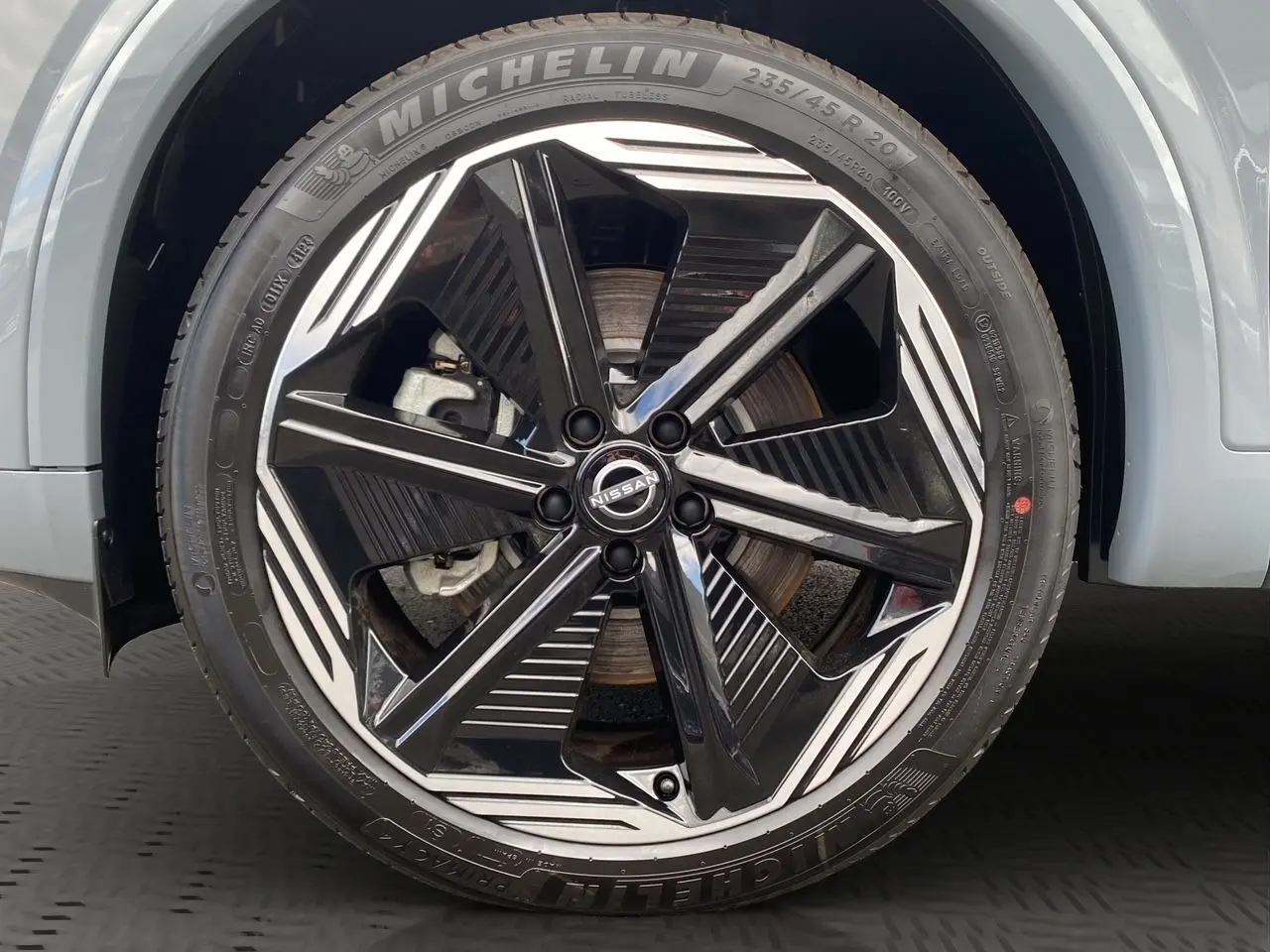 Gros plan sur la roue avant droite du Nissan Qashqai 2025 gris ceramic avec jante alliage noir et argentée au design moderne.