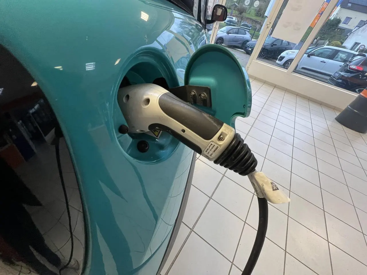 Prise de recharge branchée sur le côté gauche d'une Citroën E-MEHARI cabriolet bleu clair en intérieur showroom.