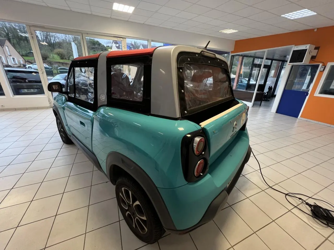 Vue 3/4 arrière droite du cabriolet Citroën E-MEHARI bleu clair avec toit en toile rouge et jantes alliage 15 pouces.