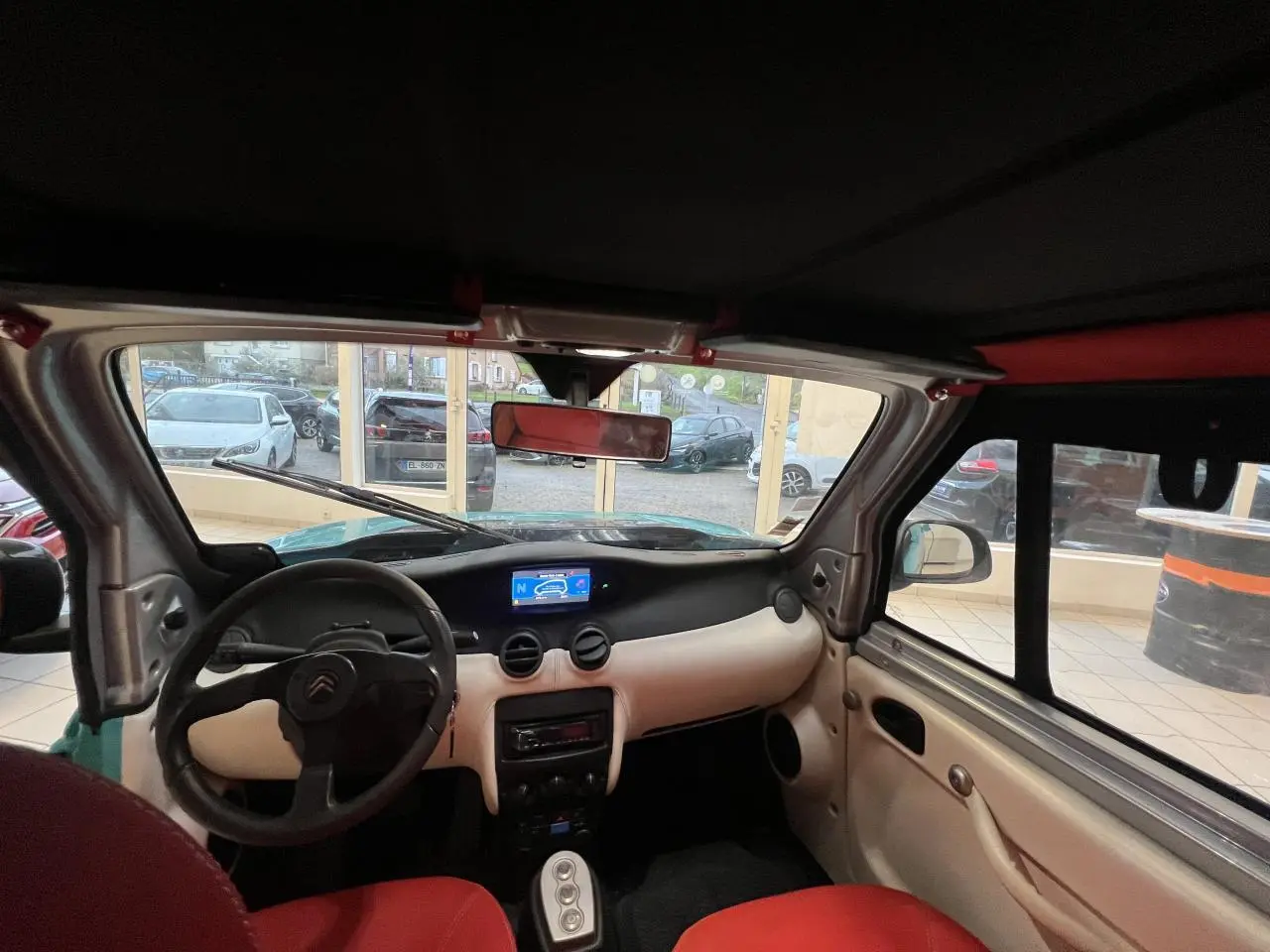 Vue intérieure avant de la Citroën E-MEHARI cabriolet bleu clair, avec tableau de bord clair et sièges rouges.