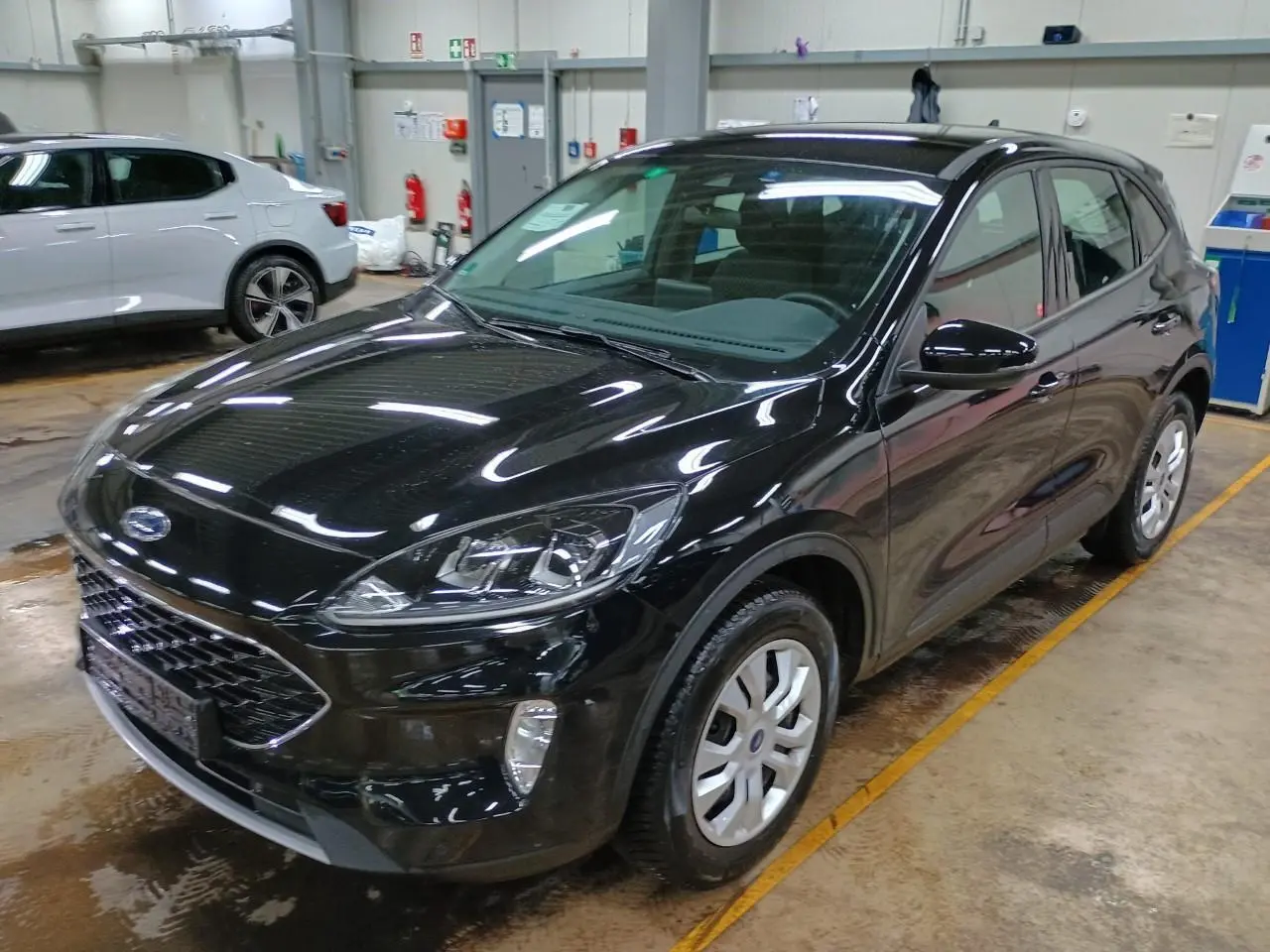 Ford Kuga noir Obsidien vu en 3/4 avant droit dans un garage, mettant en valeur ses phares et sa calandre.