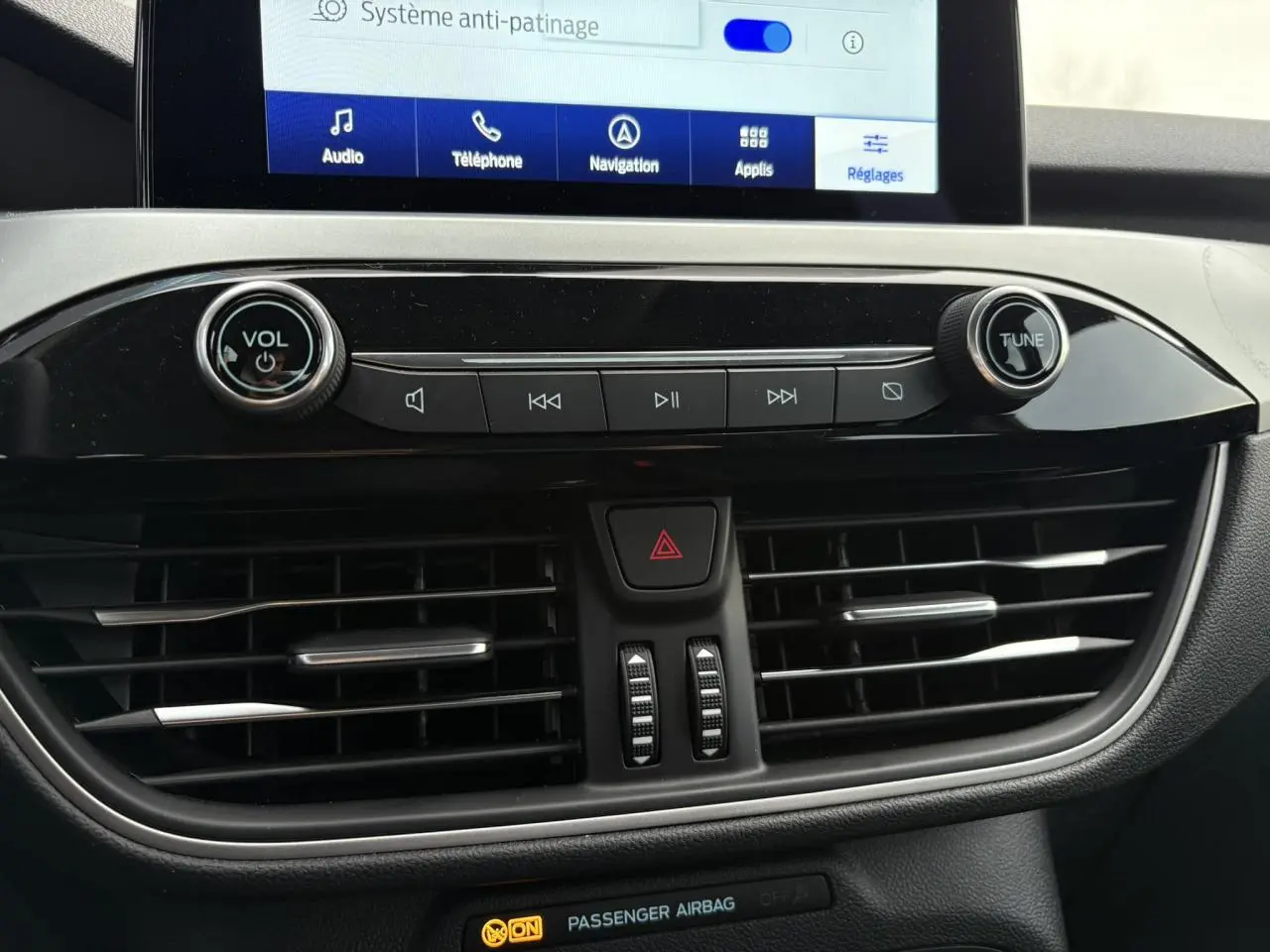 Gros plan sur la console centrale du Ford Kuga 2024 noir Obsidien, avec écran tactile et commandes audio visibles.