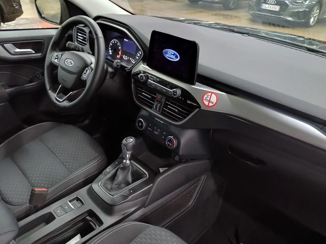 Intérieur avant droit du Ford Kuga 2024 noir Obsidien, volant cuir multifonctions et écran tactile central allumé Ford.