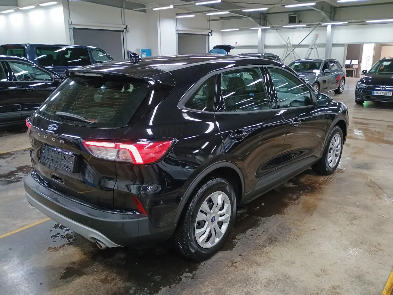 Vue 3/4 arrière droite d'un Ford Kuga 2024 noir Obsidien dans un garage, avec feux arrière allumés.
