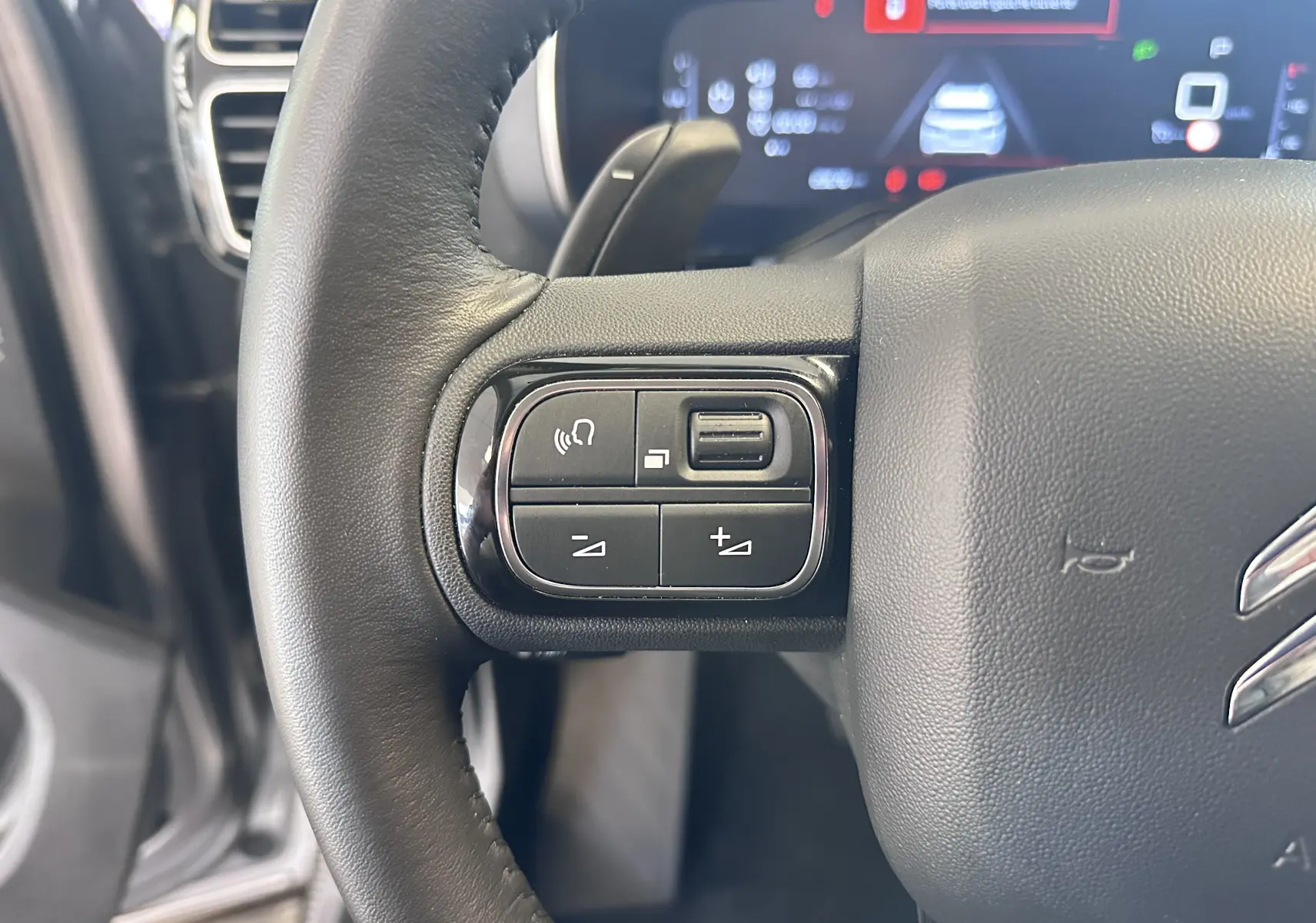 Gros plan sur les commandes gauche du volant cuir noir du Citroën C5 Aircross 2024, avec écran numérique en arrière-plan.