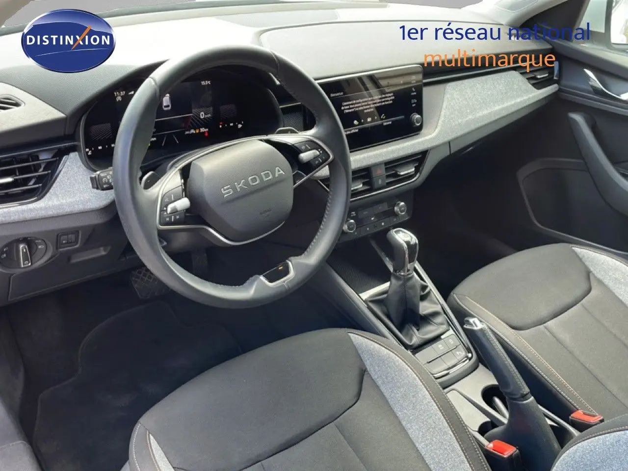 Vue intérieure de la Skoda Scala 2025, tableau de bord et volant multifonction en cuir noir avec sièges tissu gris et noir.