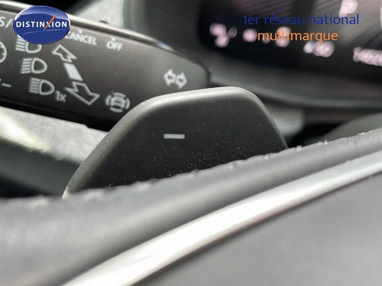 Gros plan sur la palette de changement de vitesse au volant d’une Skoda Scala blanche Glacier, avec commandes au tableau de bord floues.