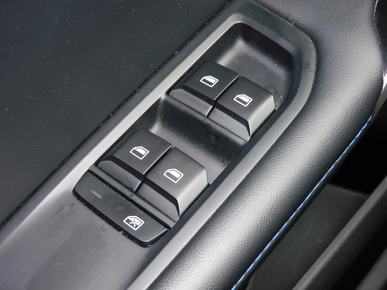 Gros plan sur les commandes de lève-vitres côté conducteur du MG4 blanc, avec surpiqûres bleues sur l'accoudoir noir.