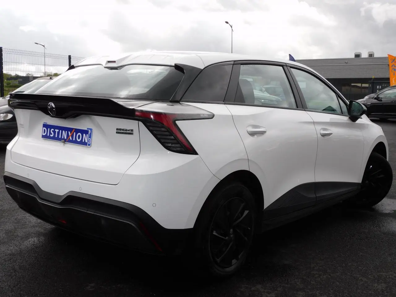 Vue 3/4 arrière droite d'une MG4 électrique blanche avec feux arrière LED et toit noir contrasté.