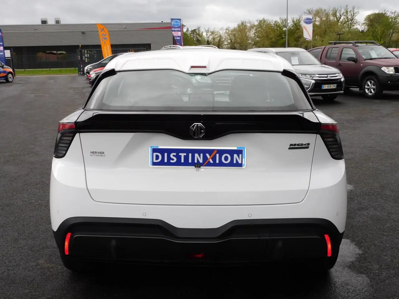 Vue arrière d'une MG4 blanche avec bande noire distinctive sur le hayon et feux arrière LED allumés.