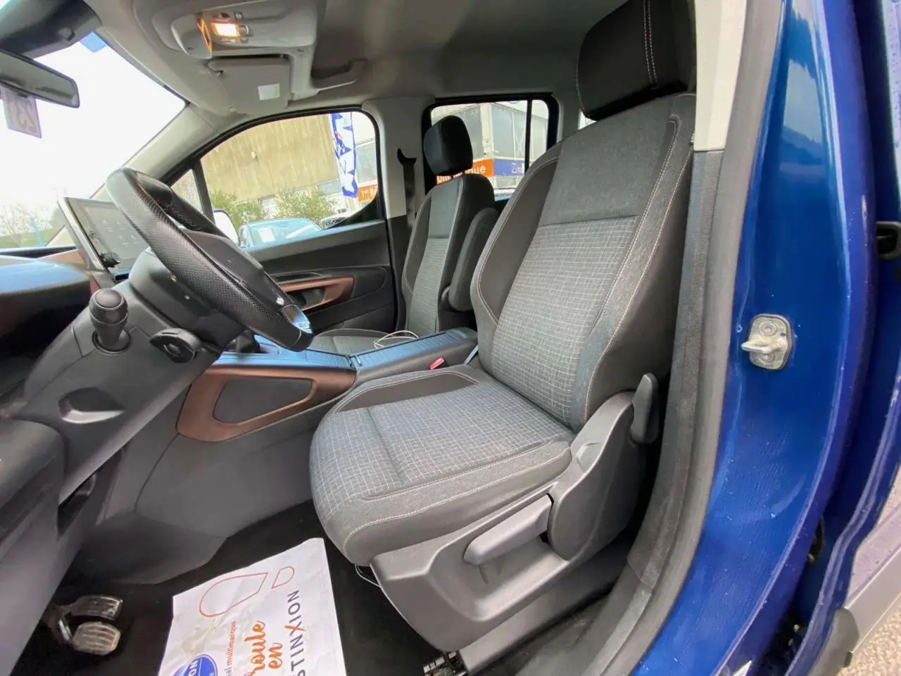 Intérieur avant du Peugeot Rifter bleu 2023, sièges tissu gris avec surpiqûres et tableau de bord visible côté conducteur.