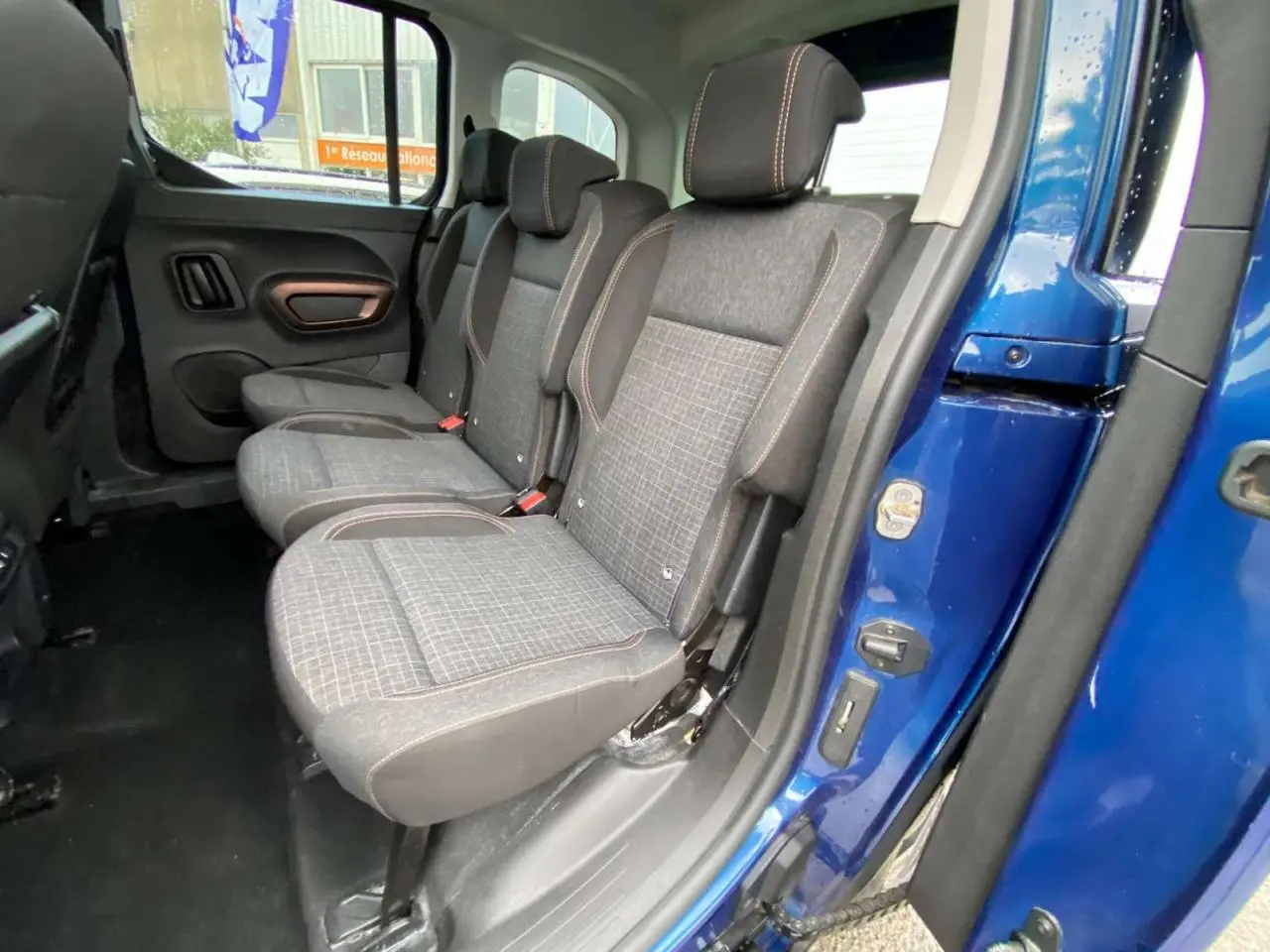 Vue latérale intérieure sur les sièges arrière gris à motifs du Peugeot Rifter GT bleu, porte ouverte côté droit.