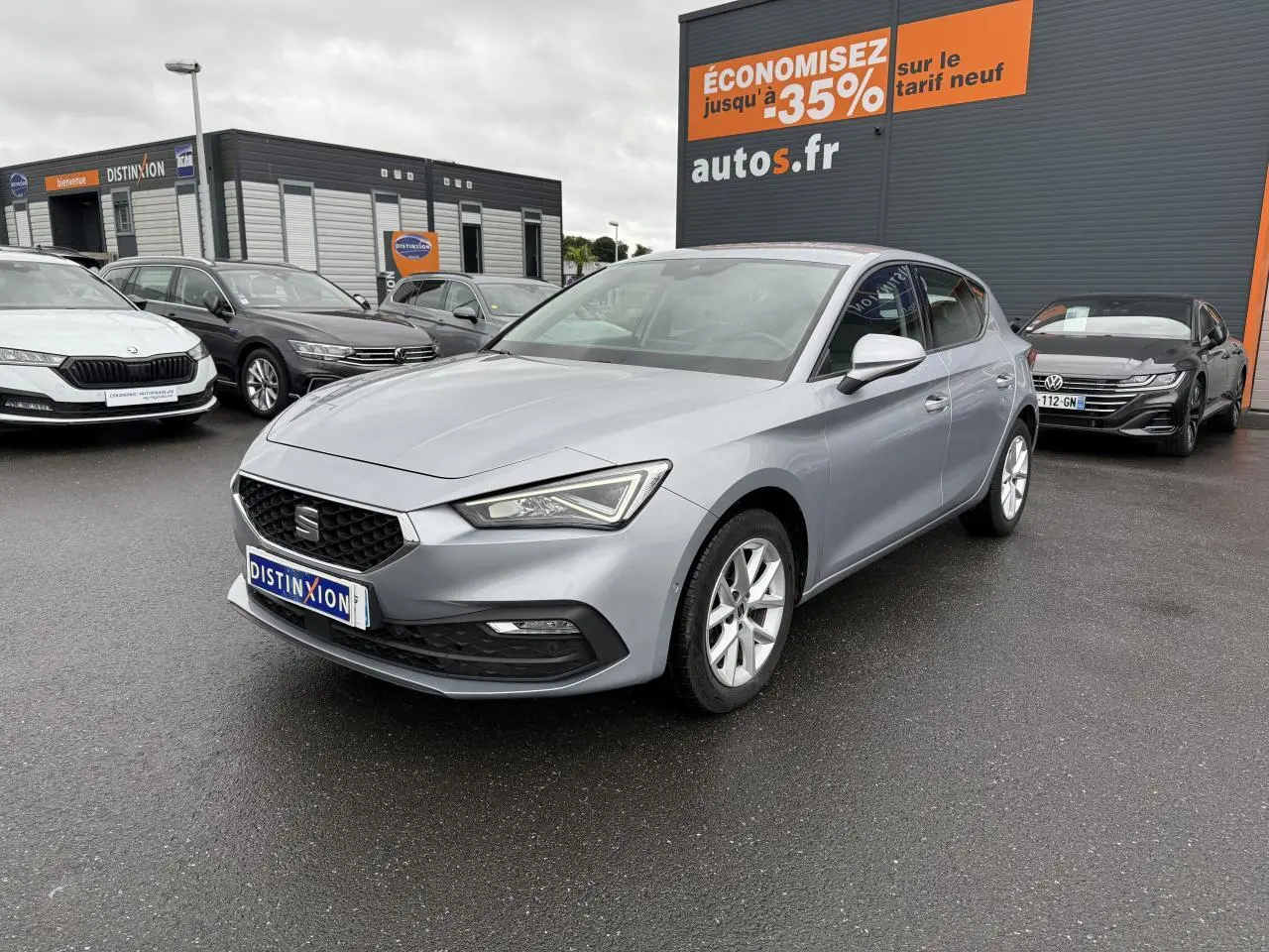 SEAT Leon 2.0 TDI 2022 en gris argenté, vue 3/4 avant droit sur parking devant un bâtiment commercial.