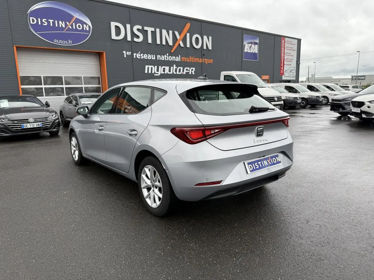 SEAT Leon 2.0 TDI 2022 en gris argenté Urban, vue 3/4 arrière droit sur parking humide devant concession.