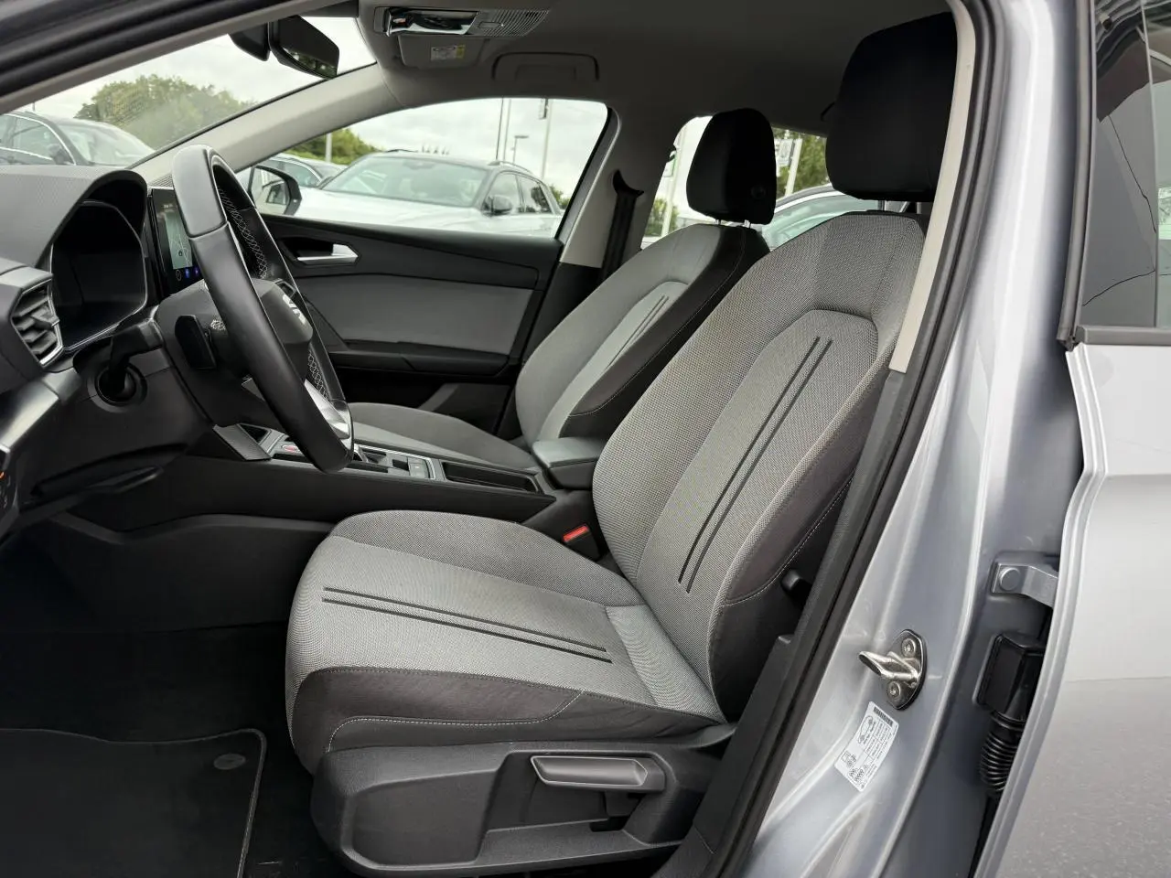 Intérieur côté conducteur d'une SEAT LEON 2022 argent Urban, avec sièges tissu gris et volant cuir multifonction.