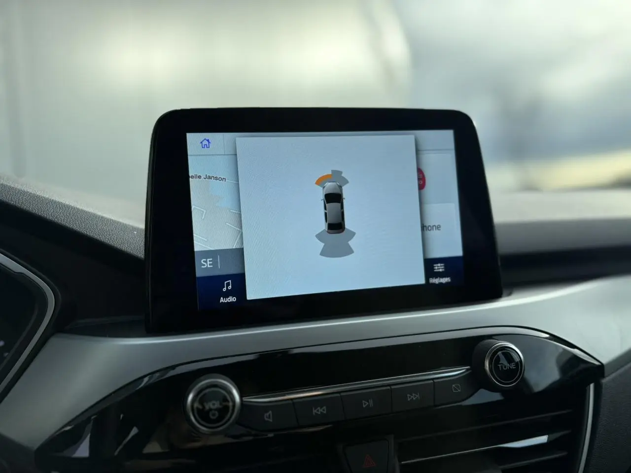 Écran tactile central du Ford Kuga 2024 affichant l'aide au stationnement avec interface moderne et tableau de bord noir.