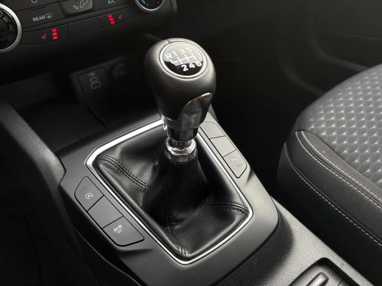 Gros plan sur la boîte manuelle et le levier de vitesse en cuir noir du Ford Kuga 2024, avec siège avant gris à motifs.