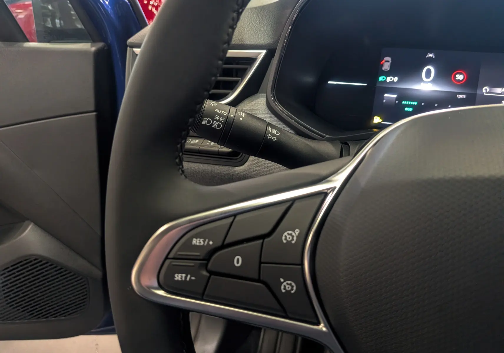 Vue intérieure rapprochée du volant noir d’une Renault Clio V Bleu Iron, avec commandes de régulateur et tableau de bord digital.