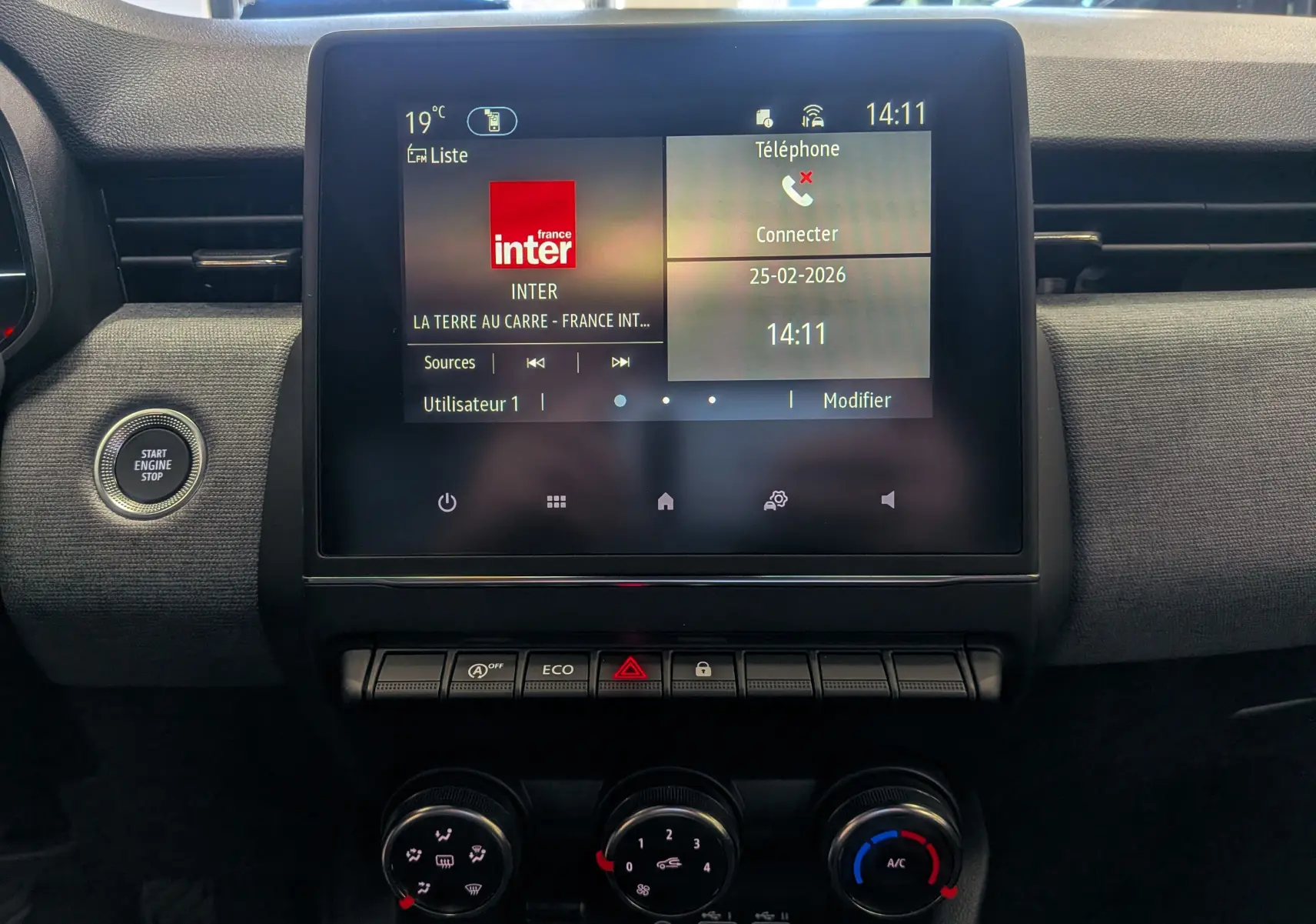 Vue rapprochée du tableau de bord de la Renault Clio V Diesel 2025, écran tactile central et commandes climatisation visibles.