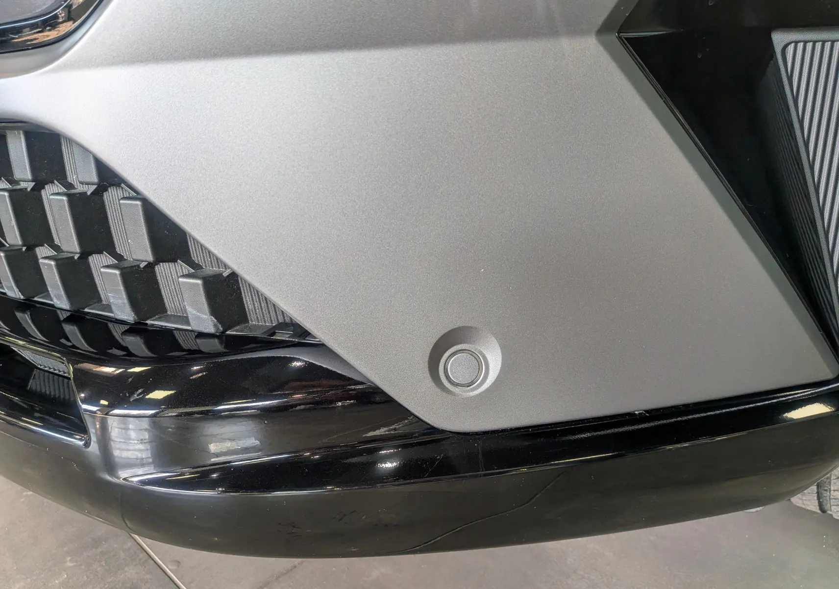 Gros plan sur le pare-chocs avant gris schiste et noir du Renault Austral E-Tech hybrid 200 Iconic esprit Alpine, avec capteur de stationnement visible.