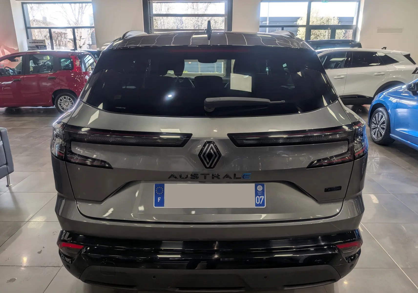 Vue arrière d’un Renault Austral E-Tech hybride 2023 gris schiste avec toit noir en showroom, détails lumineux et logo central visibles.