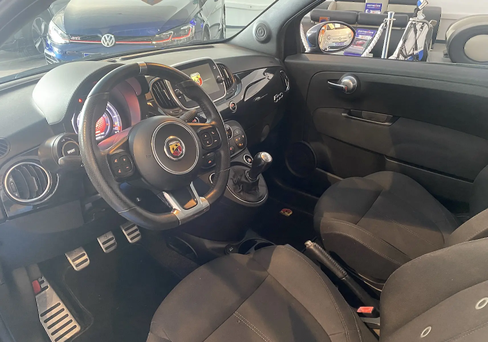 Intérieur noir de l'Abarth 595 2018 vu côté conducteur, volant sport, tableau de bord avec écran et levier de vitesse manuel.